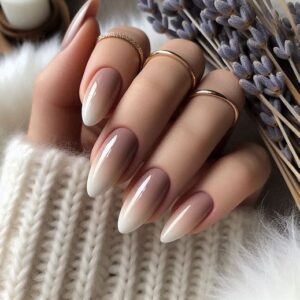 Манікюр омбре нюдових і білих тонів на довгих нігтях у поєднанні із золотими кільцями, рука на светрі, поруч лаванда.